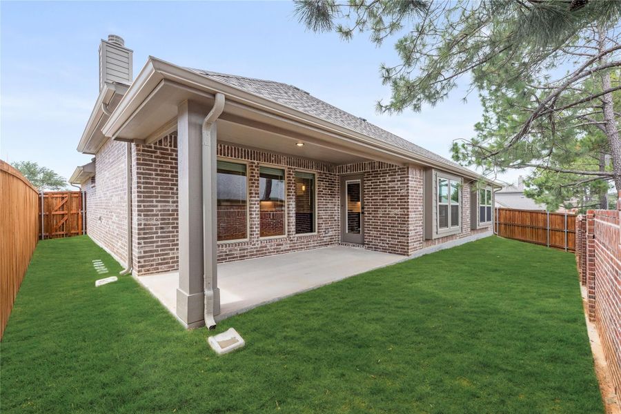Brick home rear exterior with covered patio, green lawn, and wood privacy fence