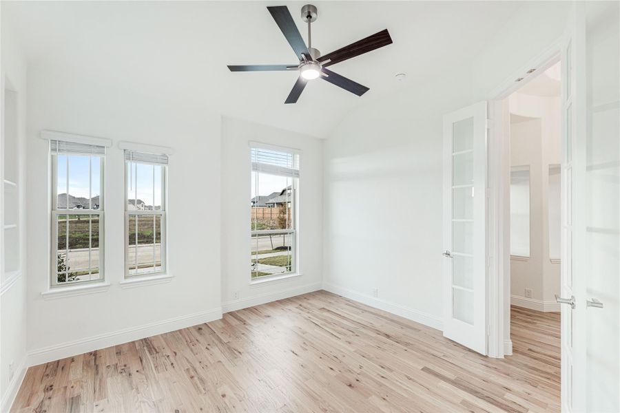 Empty bedroom with light wood floors, ceiling fan, and two windows with natural light