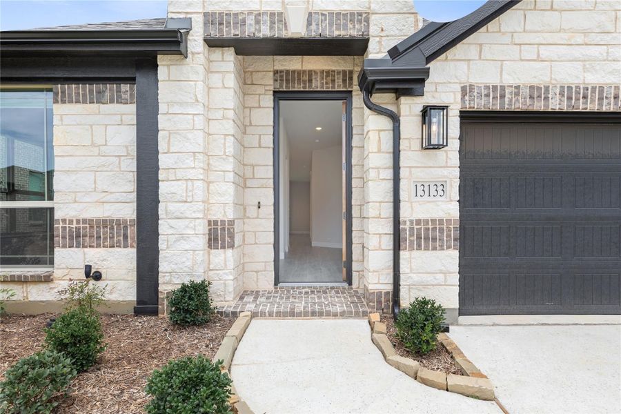 Home entrance with stone and brick exterior, dark front door, wall sconce, and attached garage at address 13133 Home entrance with stone and brick exterior, dark front door, wall sconce, and attached garage at address 13133