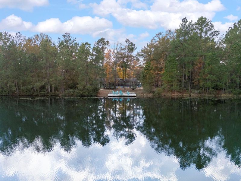 Serene lakeside view featuring a private dock with lounge chairs, surrounded by lush trees and reflecting a clear sky. Ideal for nature lovers seeking tranquility.