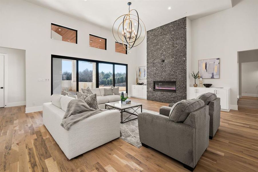 Living room with a towering ceiling, a chandelier, a fireplace, and light hardwood / wood-style floors