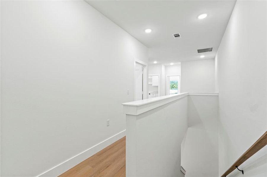 Hallway featuring light wood finished floors, an upstairs landing, and recessed lighting Hallway featuring light wood finished floors, an upstairs landing, and recessed lighting