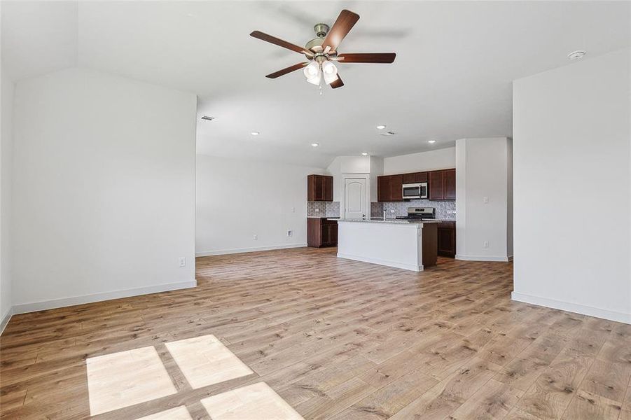 Unfurnished living room featuring vaulted ceiling, light hardwood / wood-style flooring, and ceiling fan