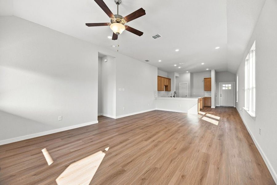 Open living area with hardwood floors, ceiling fan, and open-concept kitchen with wood cabinets in background