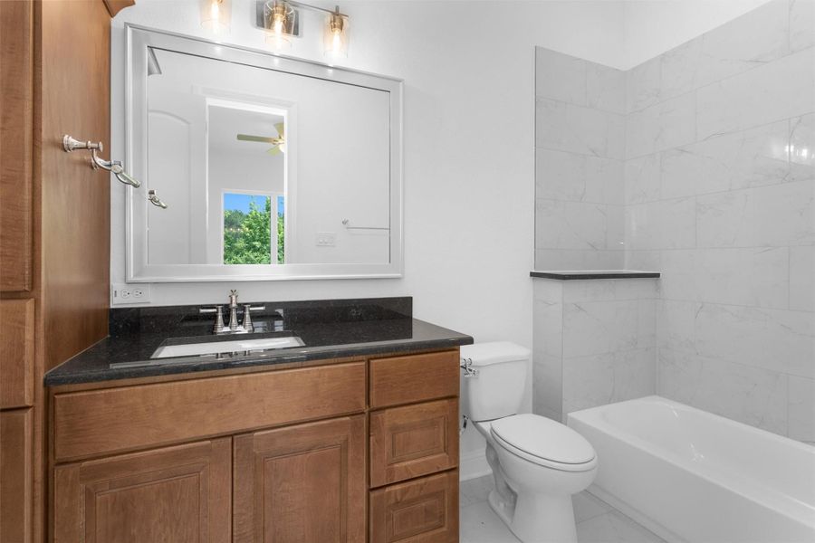Secondary bedroom includes an en-suite bathroom featuring rich wood cabinetry, granite counters, and a sleek tub-shower combo wrapped in tile. Secondary bedroom includes an en-suite bathroom featuring rich wood cabinetry, granite counters, and a sleek tub-shower combo wrapped in tile.