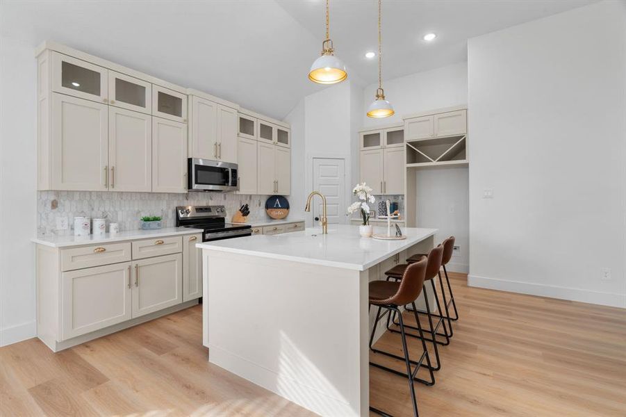 Kitchen featuring vaulted ceiling, glass insert cabinets, decorative backsplash, a breakfast bar area, and hanging light fixtures