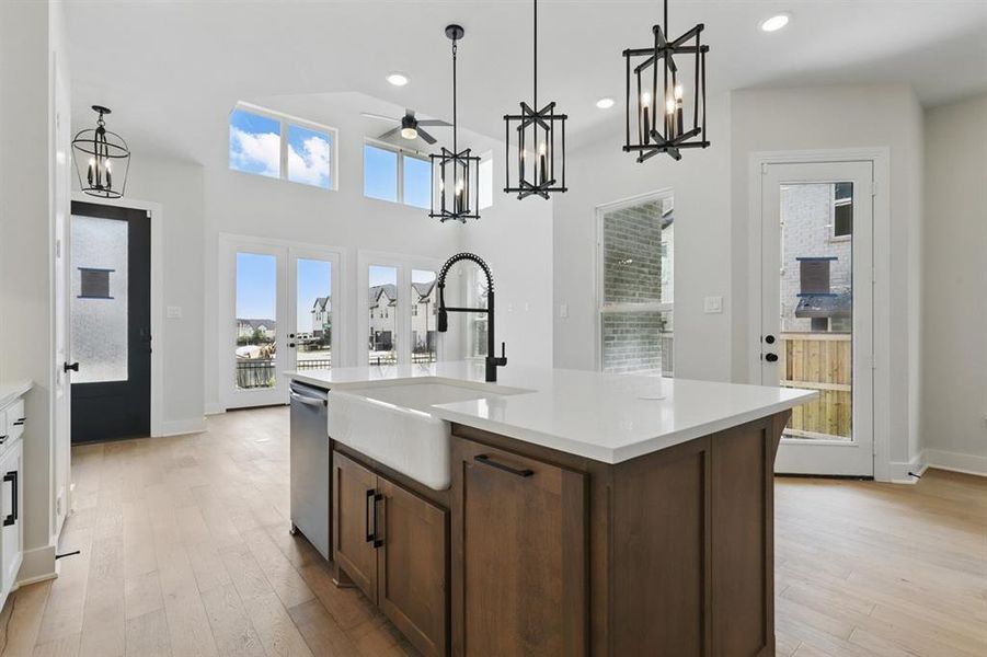 Kitchen featuring a chandelier, an island with sink, light wood-type flooring, decorative light fixtures, and dark brown cabinetry