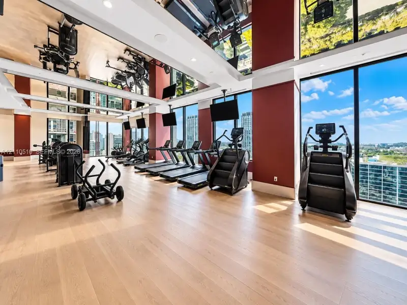 Fitness center featuring floor-to-ceiling windows, wood-finish flooring, mirrored ceiling accents, and structural columns Fitness center featuring floor-to-ceiling windows, wood-finish flooring, mirrored ceiling accents, and structural columns