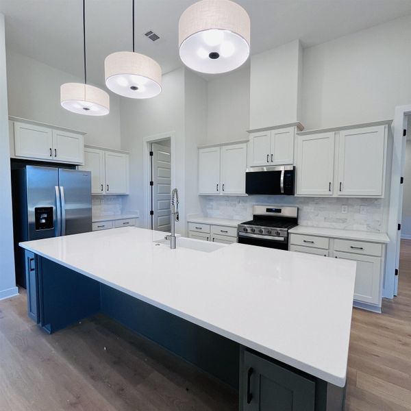 Kitchen featuring a large island with white countertop, white shaker-style cabinetry, stainless steel appliances, and a tile backsplash Kitchen featuring a large island with white countertop, white shaker-style cabinetry, stainless steel appliances, and a tile backsplash