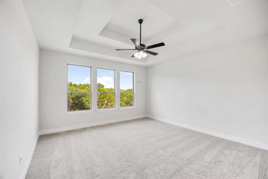 Empty room with a tray ceiling, light carpet, and a ceiling fan Empty room with a tray ceiling, light carpet, and a ceiling fan