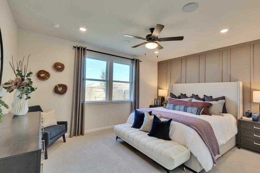 Relax in this well-lit primary bedroom featuring a designer accent wall and plush carpeting.