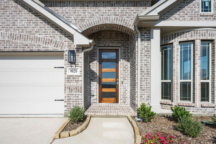 Brick home entrance with arched doorway, wood and glass front door, and attached garage