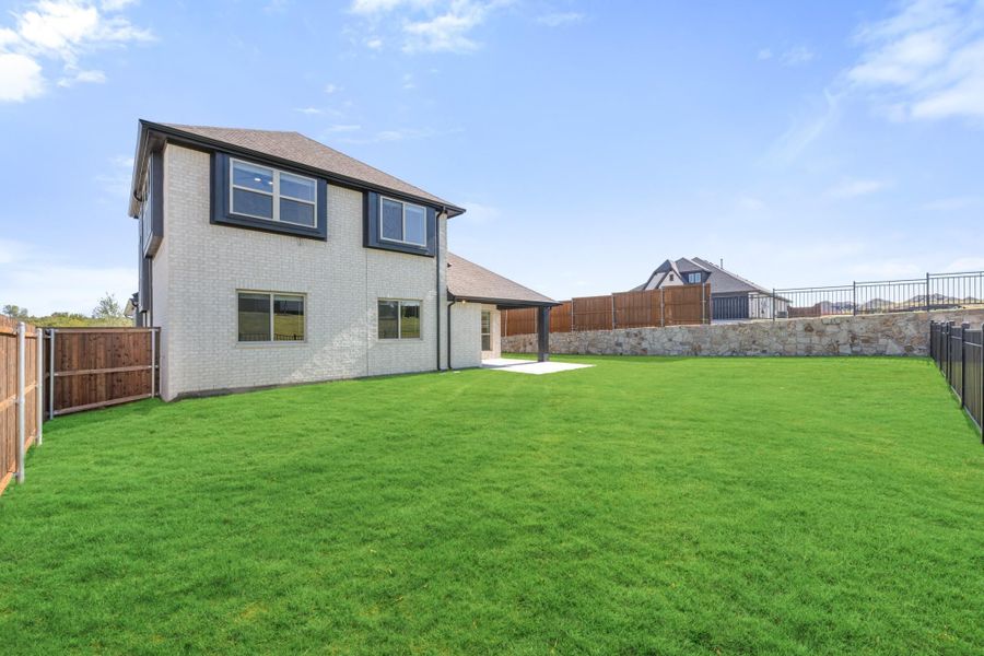 Two-story white brick home with large fenced backyard, green lawn, and covered patio area