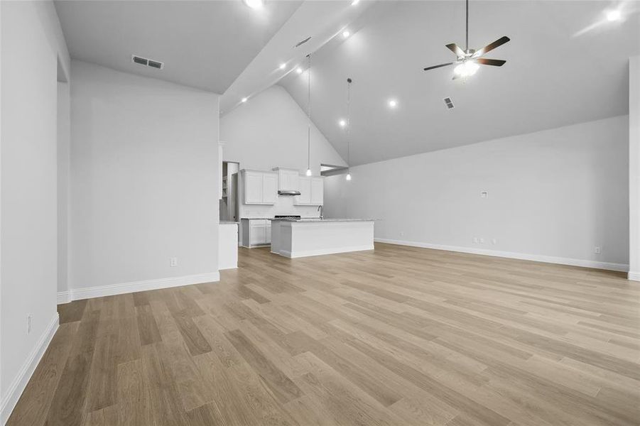 Unfurnished living room featuring high vaulted ceiling, a ceiling fan, light wood-style flooring, and baseboards Unfurnished living room featuring high vaulted ceiling, a ceiling fan, light wood-style flooring, and baseboards