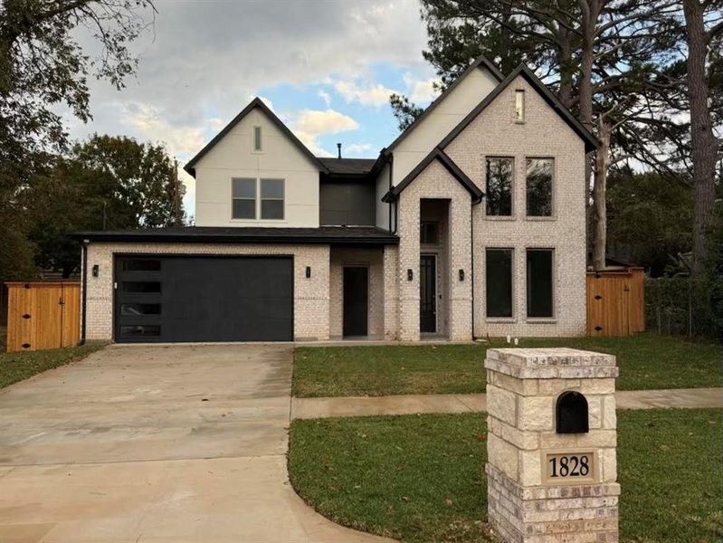 View of front of home featuring driveway, a garage, brick siding, and a gate