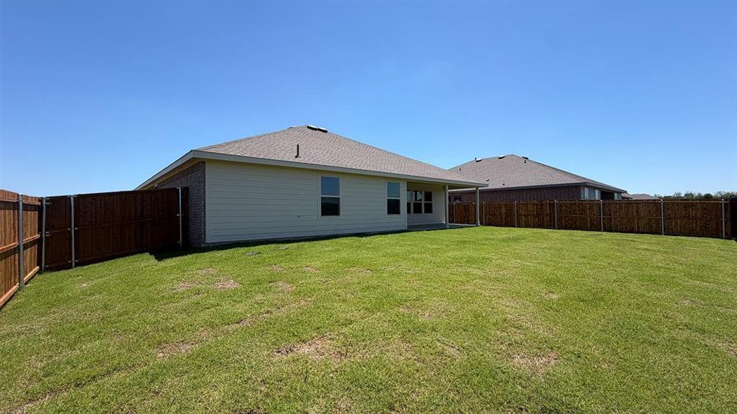 Expansive backyard featuring a manicured lawn, full privacy fencing, and a covered patio area