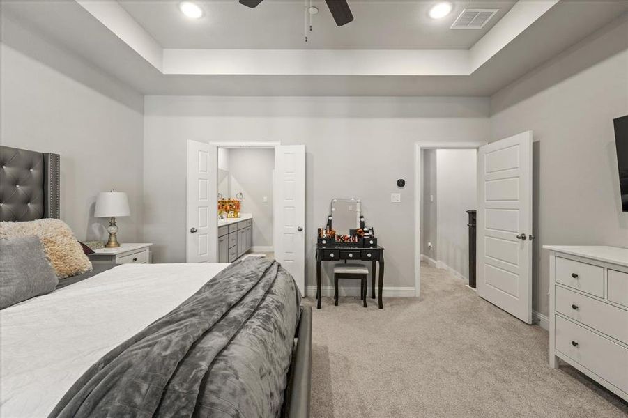 Carpeted bedroom with a raised ceiling, ensuite bath, and ceiling fan