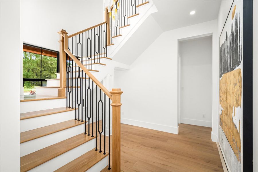 White oak statement staircase with custom iron railing, soaring ceilings, and abundant natural light, with a space for a reading nook underneath. White oak statement staircase with custom iron railing, soaring ceilings, and abundant natural light, with a space for a reading nook underneath.