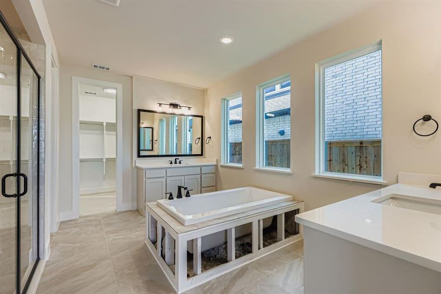 Bathroom with two vanities, a spacious closet, a soaking tub, a stall shower, and recessed lighting