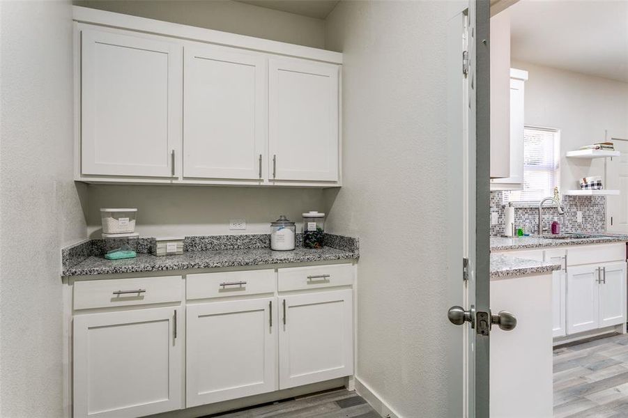 Bar featuring white cabinetry, decorative backsplash, light wood finished floors, light stone counters, and a textured wall Bar featuring white cabinetry, decorative backsplash, light wood finished floors, light stone counters, and a textured wall