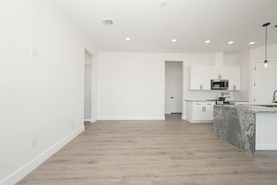This modern kitchen features white cabinetry, a sleek gray marble island with a waterfall edge, and stainless steel appliances. The space is well-lit with pendant lights and has a stylish tile backsplash. Light wood flooring adds warmth to the contemporary design.