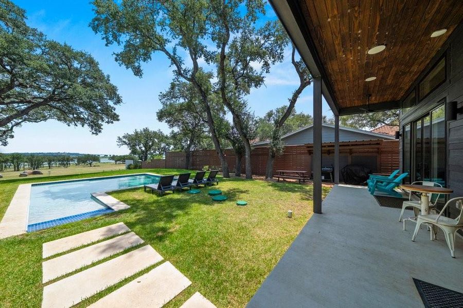 The expansive covered patio features a rich tongue-and-groove wood ceiling with recessed lighting, creating an inviting outdoor living space overlooking the pool and lake beyond. The expansive covered patio features a rich tongue-and-groove wood ceiling with recessed lighting, creating an inviting outdoor living space overlooking the pool and lake beyond.