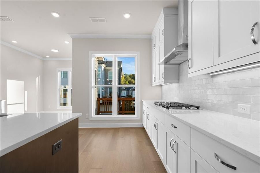 Kitchen featuring light stone counters, white cabinets, light wood-type flooring, recessed lighting, and wall chimney range hood