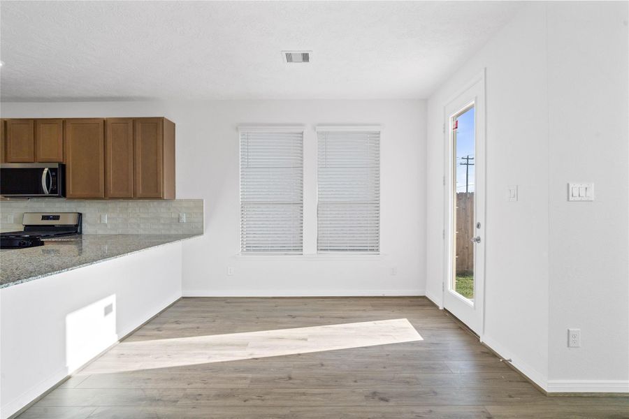 Start your day with a warm cup of coffee and quality time in this charming dining area! Highlights include large windows with blinds, custom neutral paint, vinyl plank flooring, high ceilings, and a convenient door leading to the rear patio and backyard.