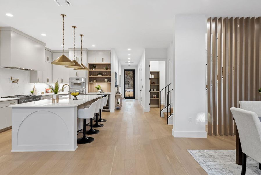 Kitchen featuring a breakfast bar, white cabinets, a center island with sink, and hanging light fixtures