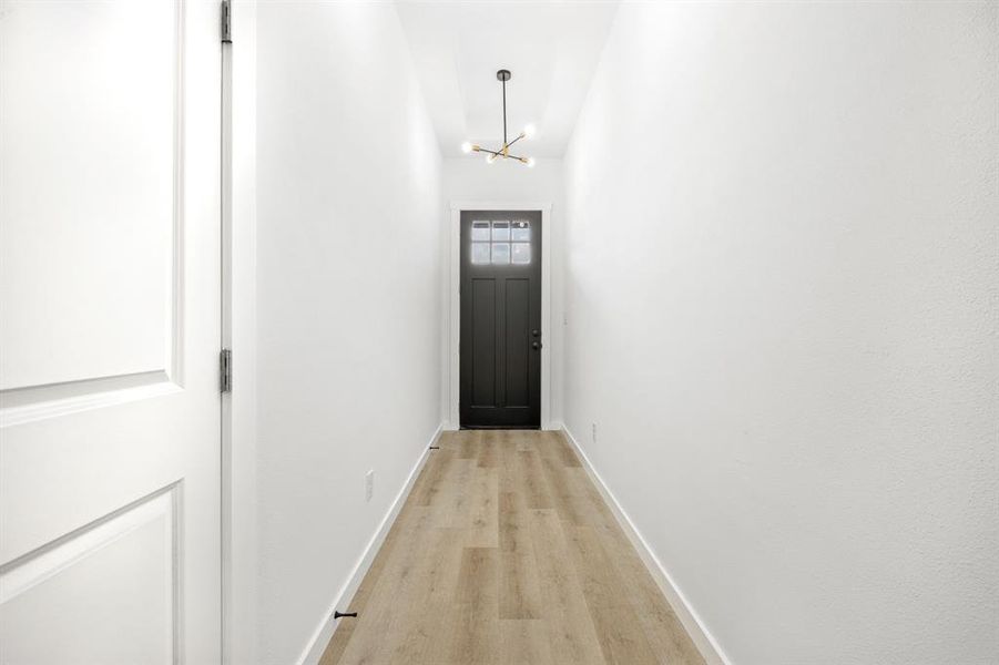 Doorway with a notable chandelier and light wood-type flooring