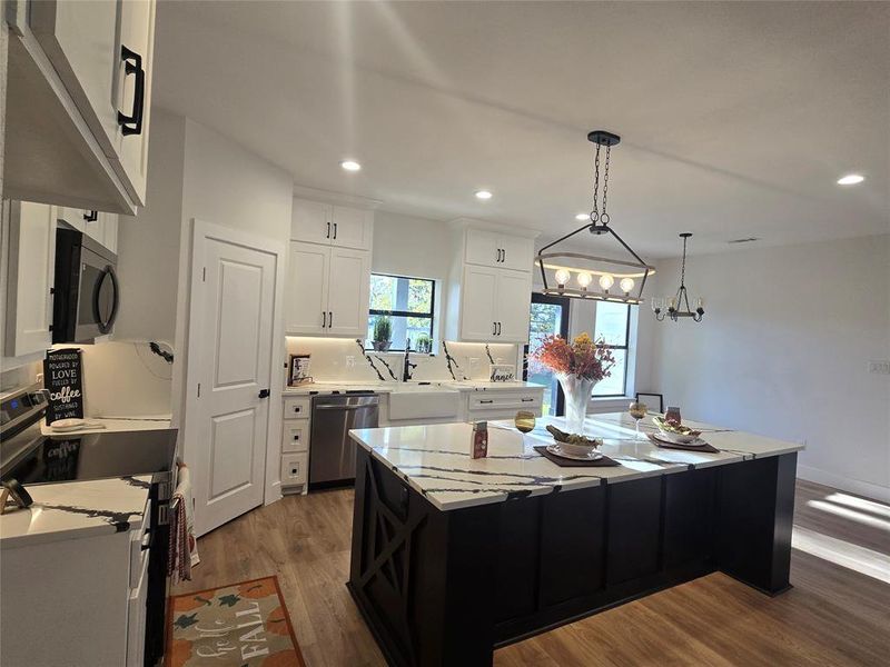 Kitchen with dark cabinetry, stainless steel appliances, white cabinetry, hanging light fixtures, and a center island