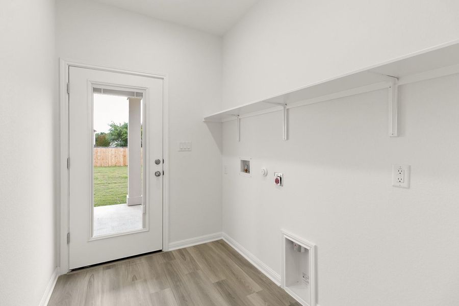 Utility area featuring light wood-style flooring, white walls, and an exterior door providing access to the yard
