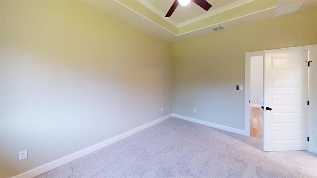 Empty room featuring ceiling fan, light colored carpet, baseboards, and a raised ceiling