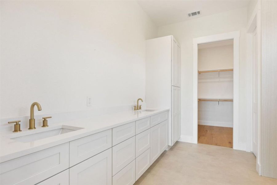 Dual vanities with golden fixtures grace this ample bathroom, leading to a convenient walk-in closet. Dual vanities with golden fixtures grace this ample bathroom, leading to a convenient walk-in closet.