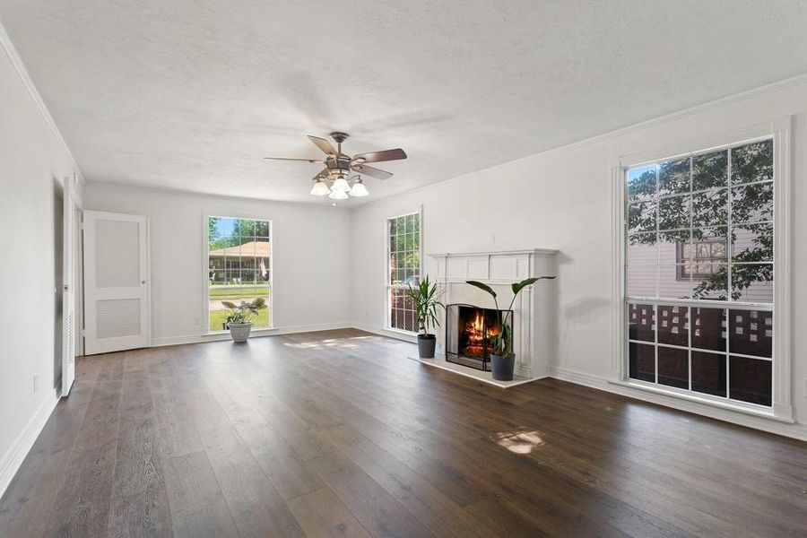 Unfurnished living room with hardwood / wood-style floors, ceiling fan, a lit fireplace, baseboards, and ornamental molding
