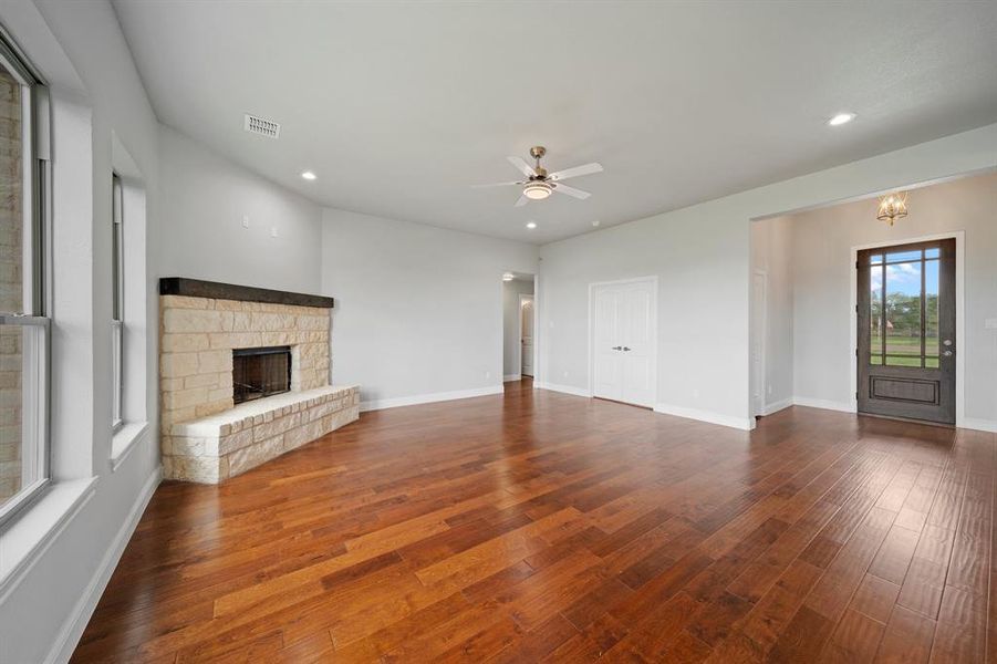 Unfurnished living room with a fireplace, ceiling fan with notable chandelier, and hardwood / wood-style floors