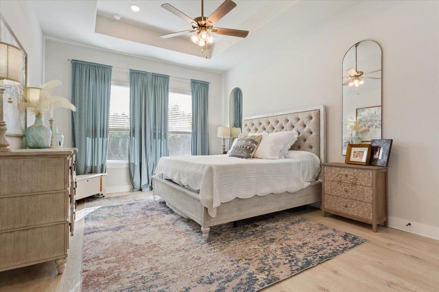 Bedroom featuring a raised ceiling, a ceiling fan, and light wood-type flooring