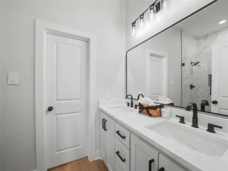 Dual vanity featuring white shaker-style cabinetry, white countertops with integrated sinks, and matte black plumbing fixtures Dual vanity featuring white shaker-style cabinetry, white countertops with integrated sinks, and matte black plumbing fixtures