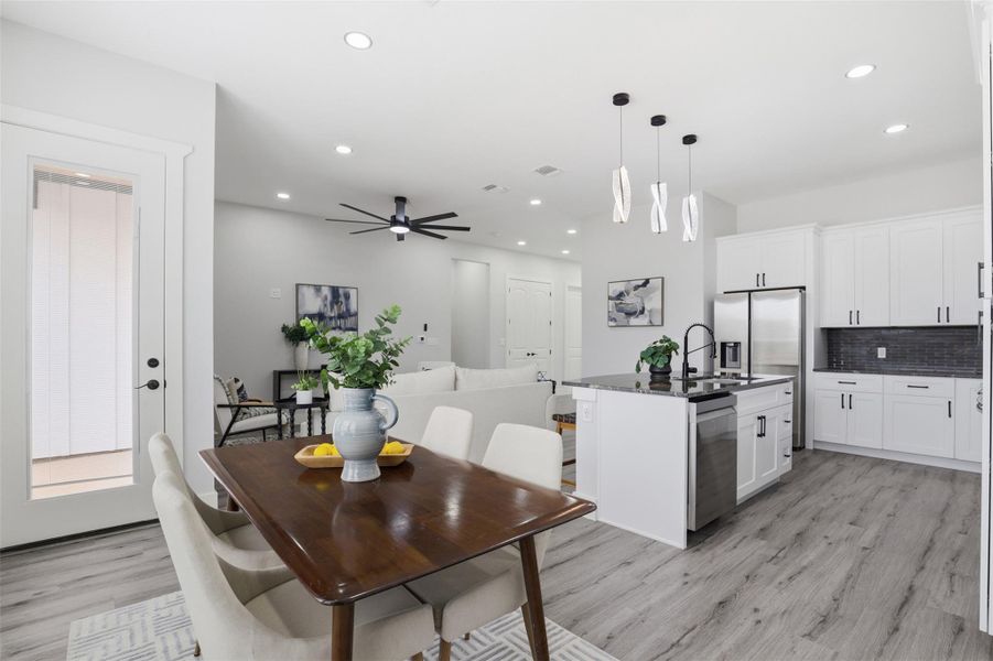 Open-concept living space featuring wood-finish flooring, white cabinetry, stainless steel appliances, and a kitchen island with pendant lighting