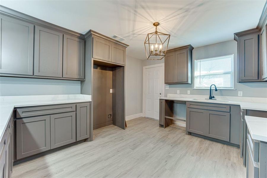 Kitchen featuring sink, gray cabinetry, light wood-type flooring, and decorative light fixtures