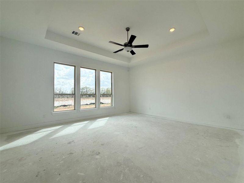 As you enter the primary bedroom, you’re greeted by an abundance of natural light pouring in through large, beautifully framed windows, casting a warm glow on the soft, neutral tones of the walls.