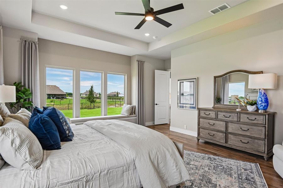Master bedroom with tray ceiling, ceiling fan, hardwood floors, and large windows with backyard view Master bedroom with tray ceiling, ceiling fan, hardwood floors, and large windows with backyard view