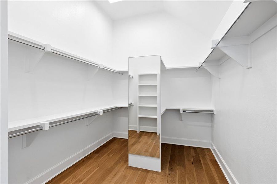 Walk-in closet featuring wood-finish flooring, crisp white walls, extensive shelving, integrated hanging rods, and a full-length mirror