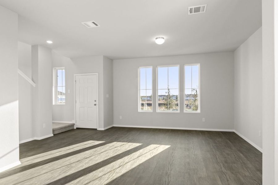 Image of a living room with brown wood-like flooring with light grey painted walls with three windows