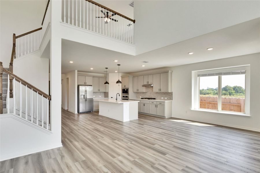 Unfurnished living room featuring a high ceiling, light wood-style flooring, stairs, and recessed lighting