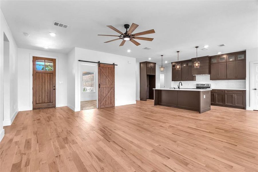 Kitchen with a kitchen island with sink, light hardwood / wood-style floors, pendant lighting, a barn door, and backsplash Kitchen with a kitchen island with sink, light hardwood / wood-style floors, pendant lighting, a barn door, and backsplash