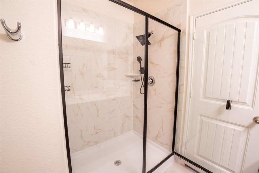 Modern shower enclosure featuring a black-framed glass door, marble-patterned tile surround, and a white shower pan Modern shower enclosure featuring a black-framed glass door, marble-patterned tile surround, and a white shower pan