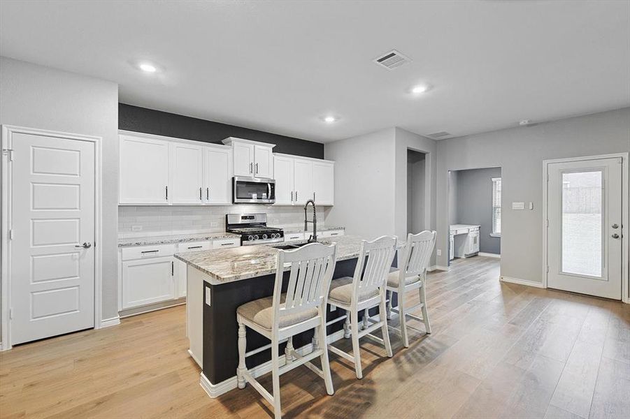 Kitchen with light stone counters, stainless steel appliances, an island with sink, and white cabinets