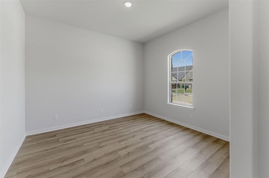 Room featuring wood-finish flooring, white baseboards, and a single arched window with grid panes Room featuring wood-finish flooring, white baseboards, and a single arched window with grid panes