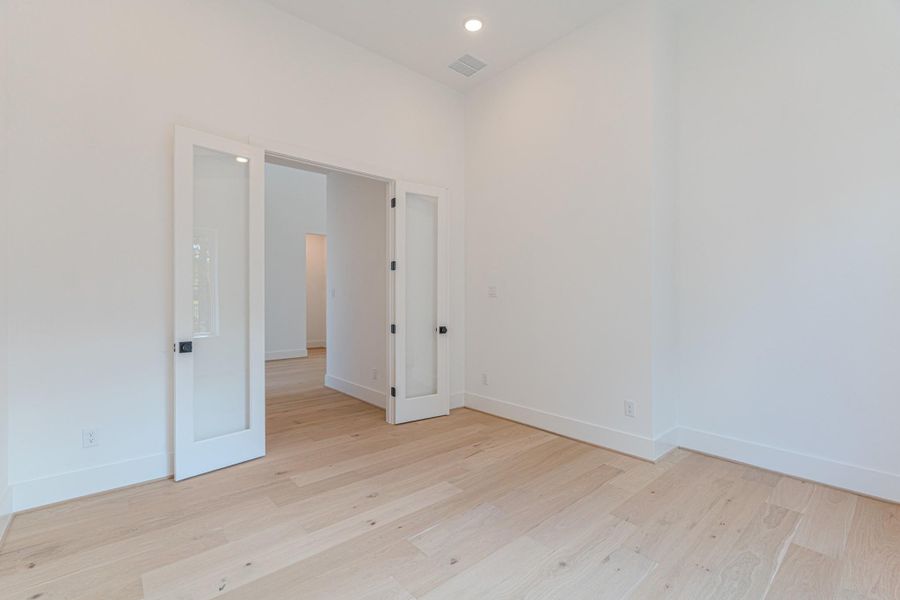 This room features light wood flooring and bright white walls, creating an open and airy feel. It includes double glass doors leading to another space, enhancing the flow of natural light.